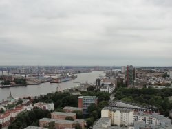 Blick entlang der Elbe mit Landungsbrücken und Hochhäusern auf dem rechten Ufer, Schwimmdocks und Booten auf dem Wasser und zahlreichen Containerbrücken am linken Ufer
